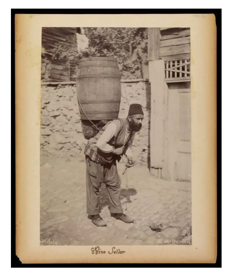 Sepia studio photograph of an Ottoman-era porter carrying a large barrel strapped to his back
