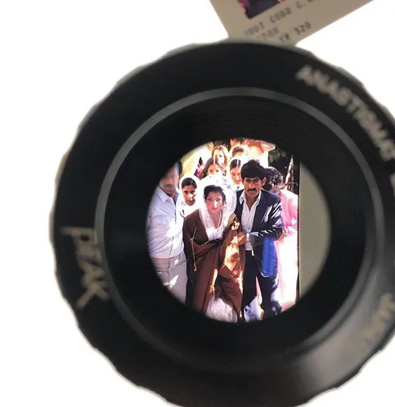 A photographic slide seen through a loupe: a wedding procession, a man in a suit beside a woman in a sari.